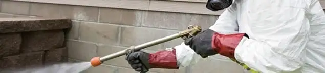 Pest control technician applying exterior insect treatment along a home foundation in Evansville, IN