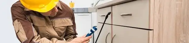 Roach exterminator applying treatment under kitchen cabinets in Evansville, IN