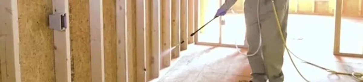 Termite treatment technician applying spray along framing and unfinished walls in Evansville, IN