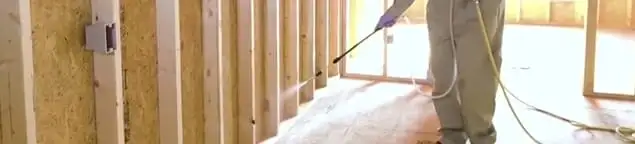 Termite treatment technician applying spray along framing and unfinished walls in Evansville, IN